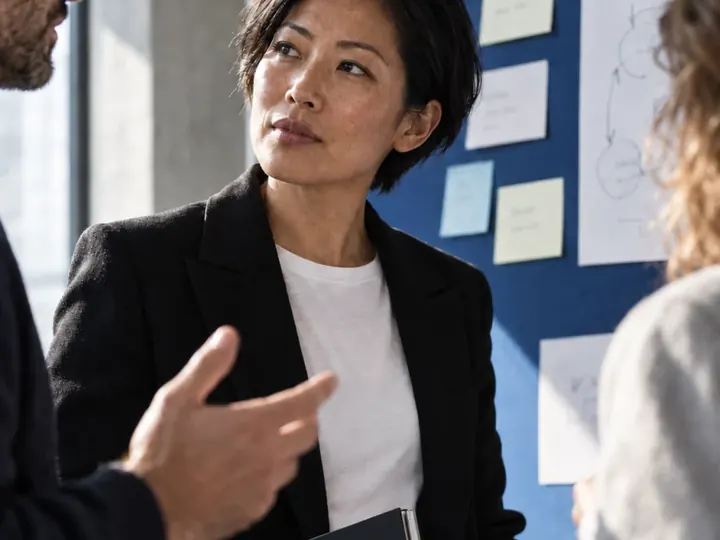 A woman presenting to colleagues in front of a pinboard of notes.