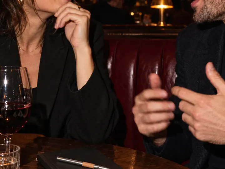 Two people laughing over dinner, the pen resting on a closed notebook.