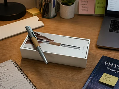 A study desk with revision notes on sticky pads, a laptop and the Scriben pen in its open box